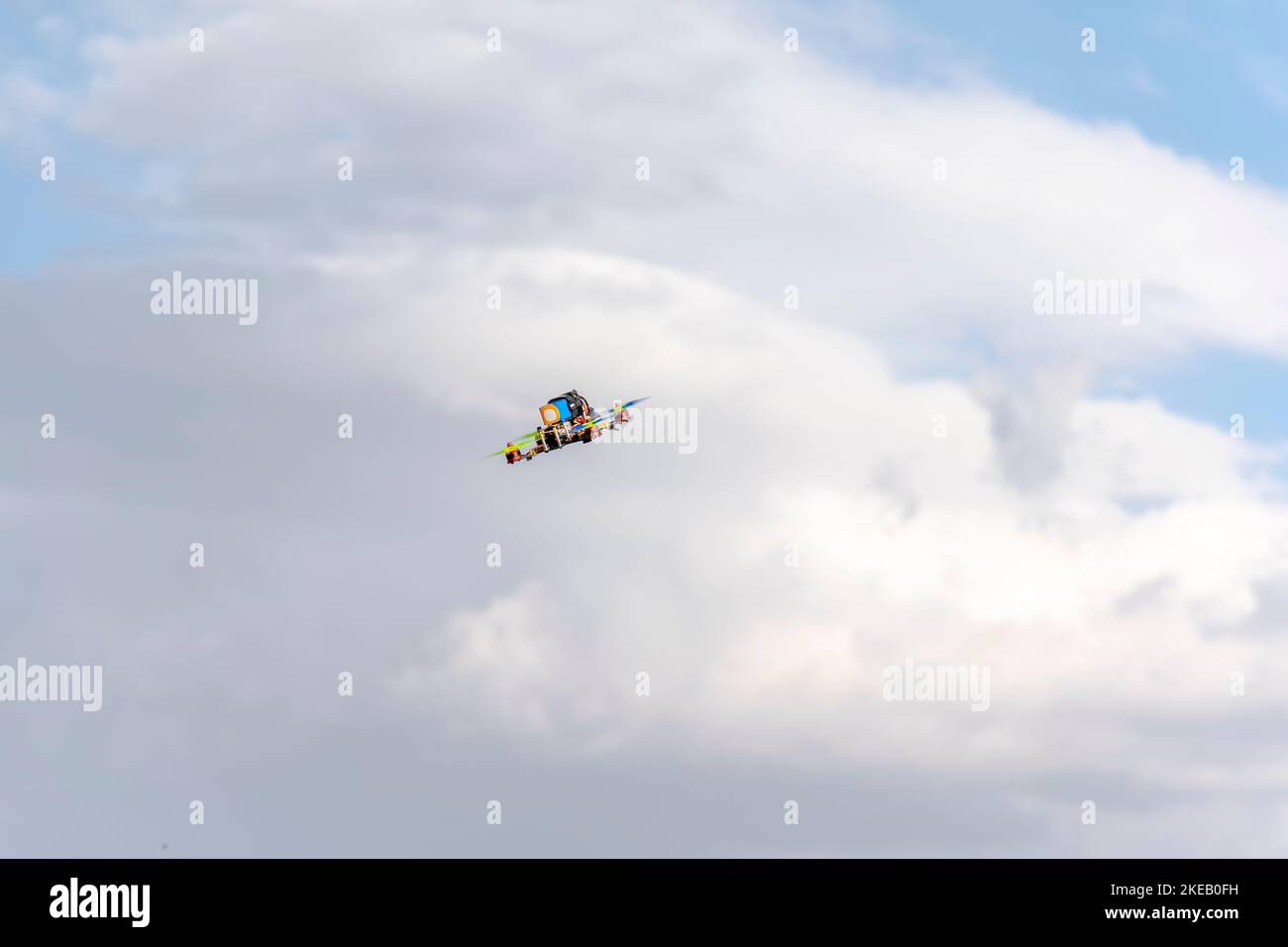 Drone quadricottero volante con cielo nuvoloso blu sullo sfondo. Vista dall'angolo basso del veicolo multicolore senza equipaggio in aria. Foto Stock