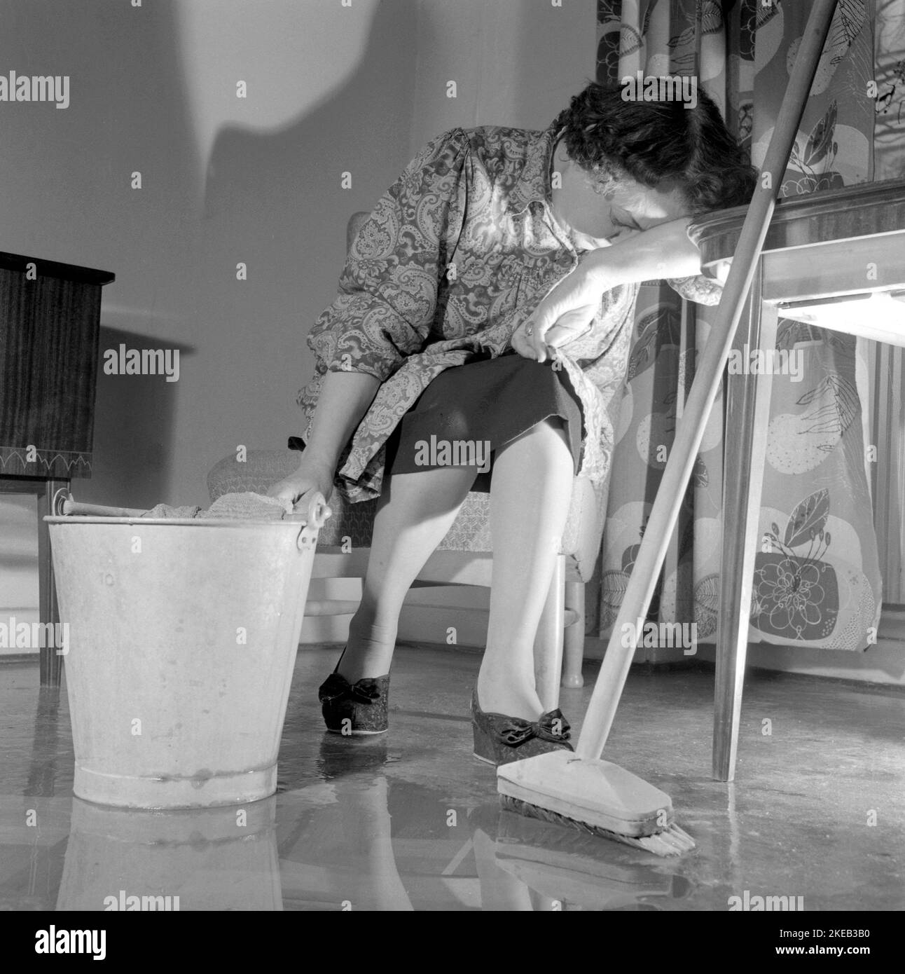 Pulire il pianale sul retro. Una donna sembra molto stanca e logora quando si siede su una sedia, avendo un riposo nel lavoro di pulizia dei pavimenti. Svezia 1956 Conard Ref 3160 Foto Stock