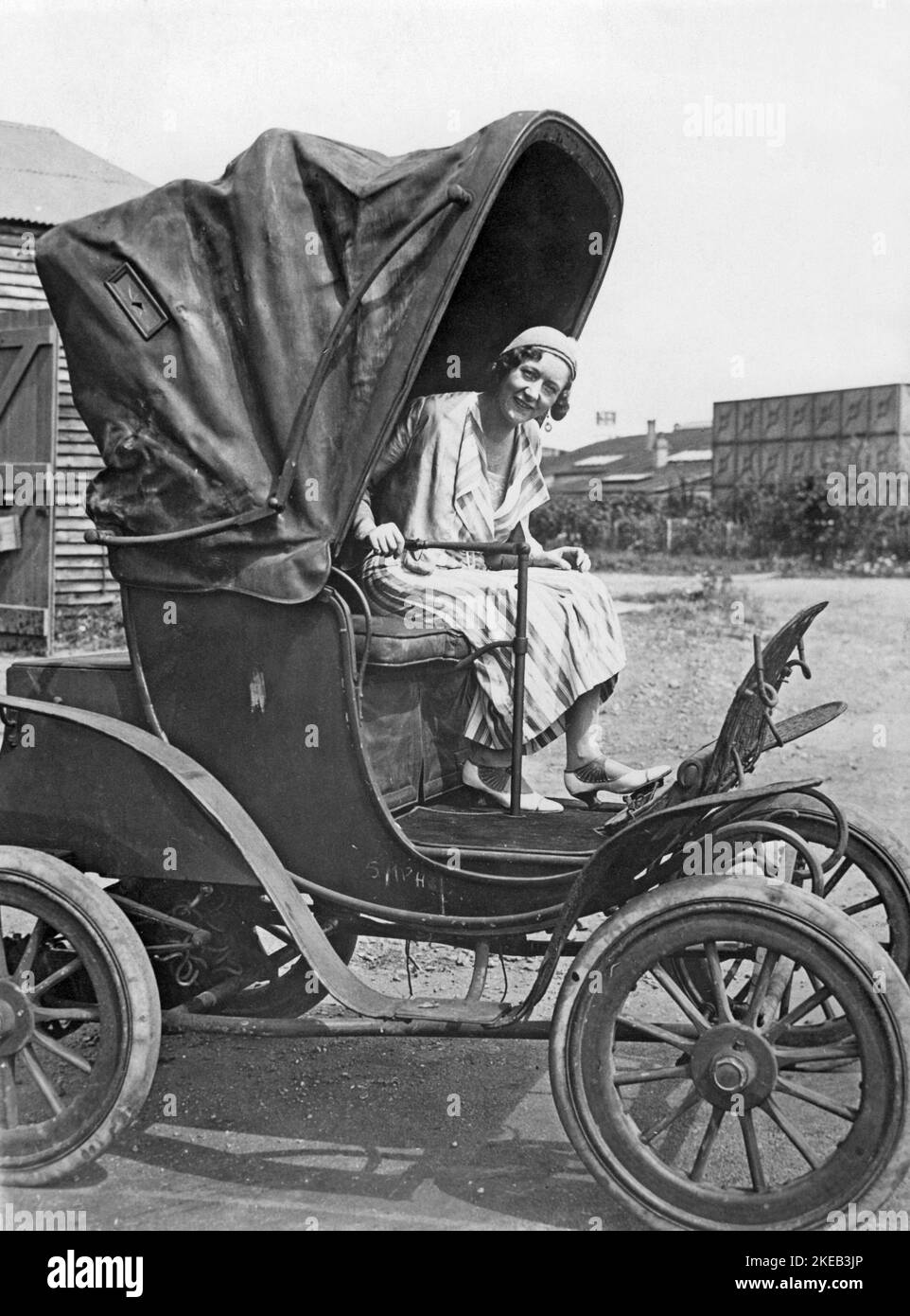 Auto elettriche negli anni '1930s. Una donna seduta sul sedile del conducente in un'auto elettrica. Un primo modello che ha due sedili con nulla per proteggere dalla pioggia, tranne un grande cofano. Lo sterzo della vettura è una semplice leva. 1930s Foto Stock