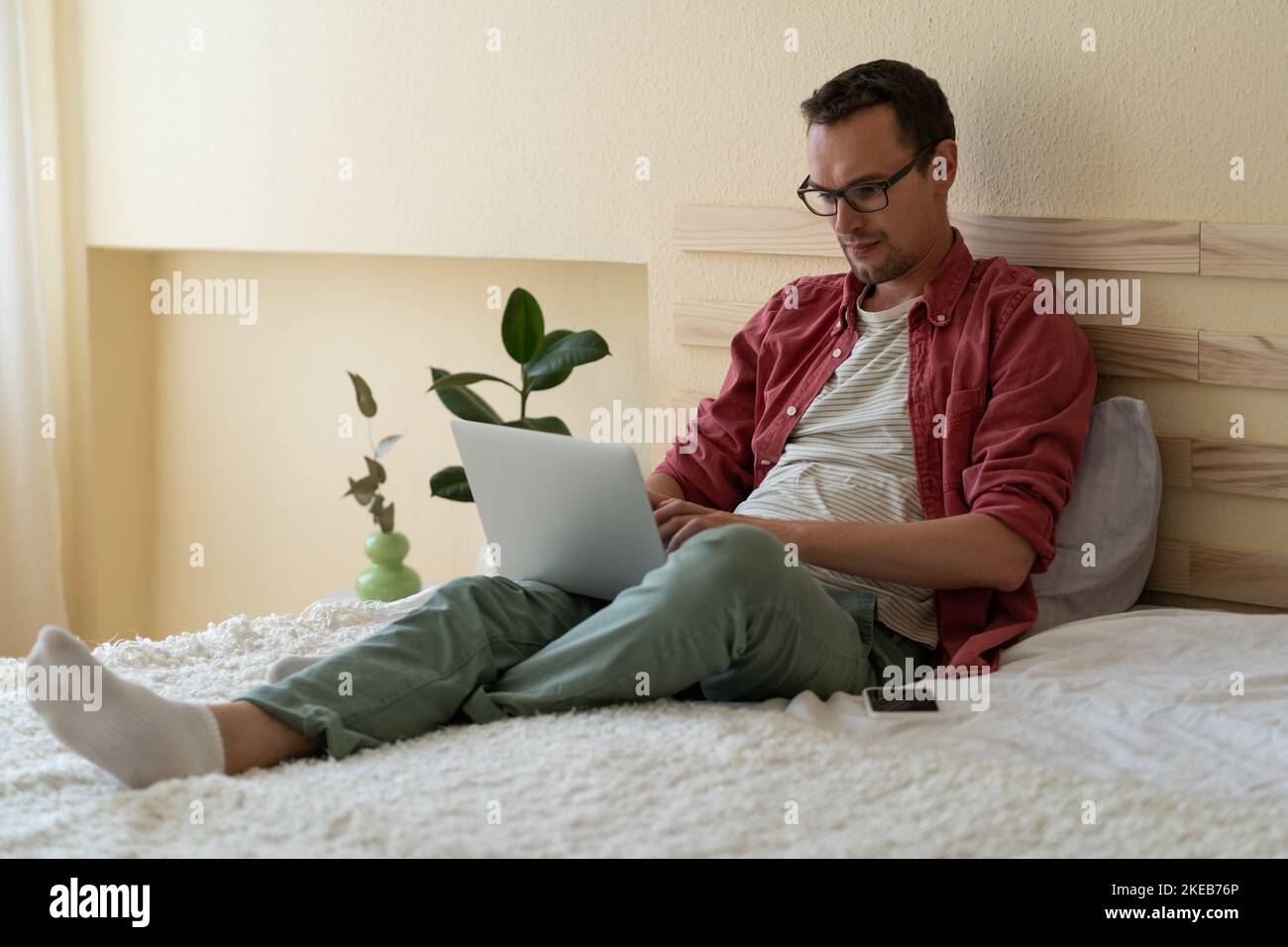 L'uomo caucasico concentrato si siede sul letto nella camera dell'hotel leggendo le notizie via internet o controllando la posta elettronica Foto Stock