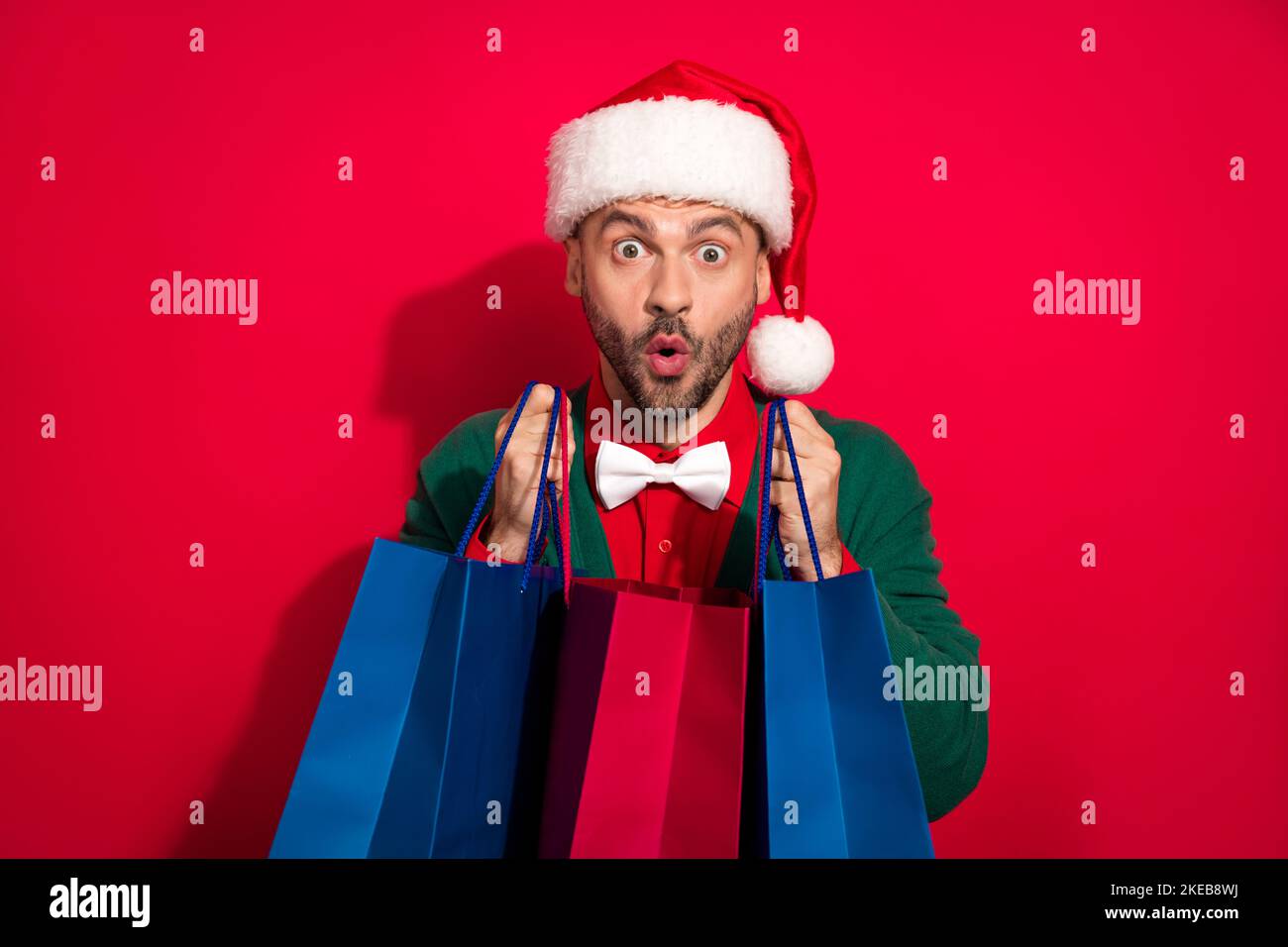 Foto del tipo eccitato funky vestito xmas verde cardigan bowtie ottenere noel regali acquirenti isolato sfondo di colore rosso Foto Stock