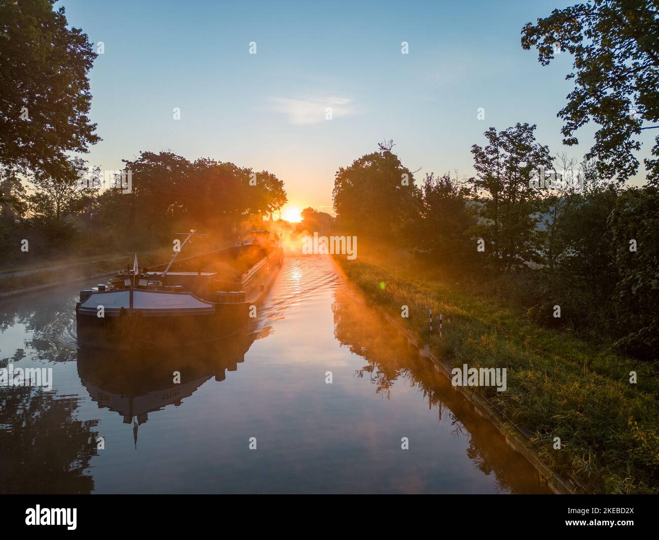 Vista aerea di un colorato e suggestivo cielo all'alba su un canale con una barca da carico in Belgio. Canali con acqua per i trasporti, l'agricoltura. Campi e prati. Vista aerea panoramica ripresa da un drone. Foto di alta qualità Foto Stock