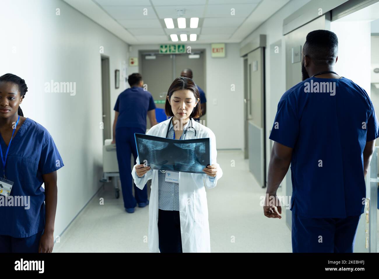 Medico asiatico femminile che studia foto radiografica in piedi in corridoio occupato ospedale Foto Stock