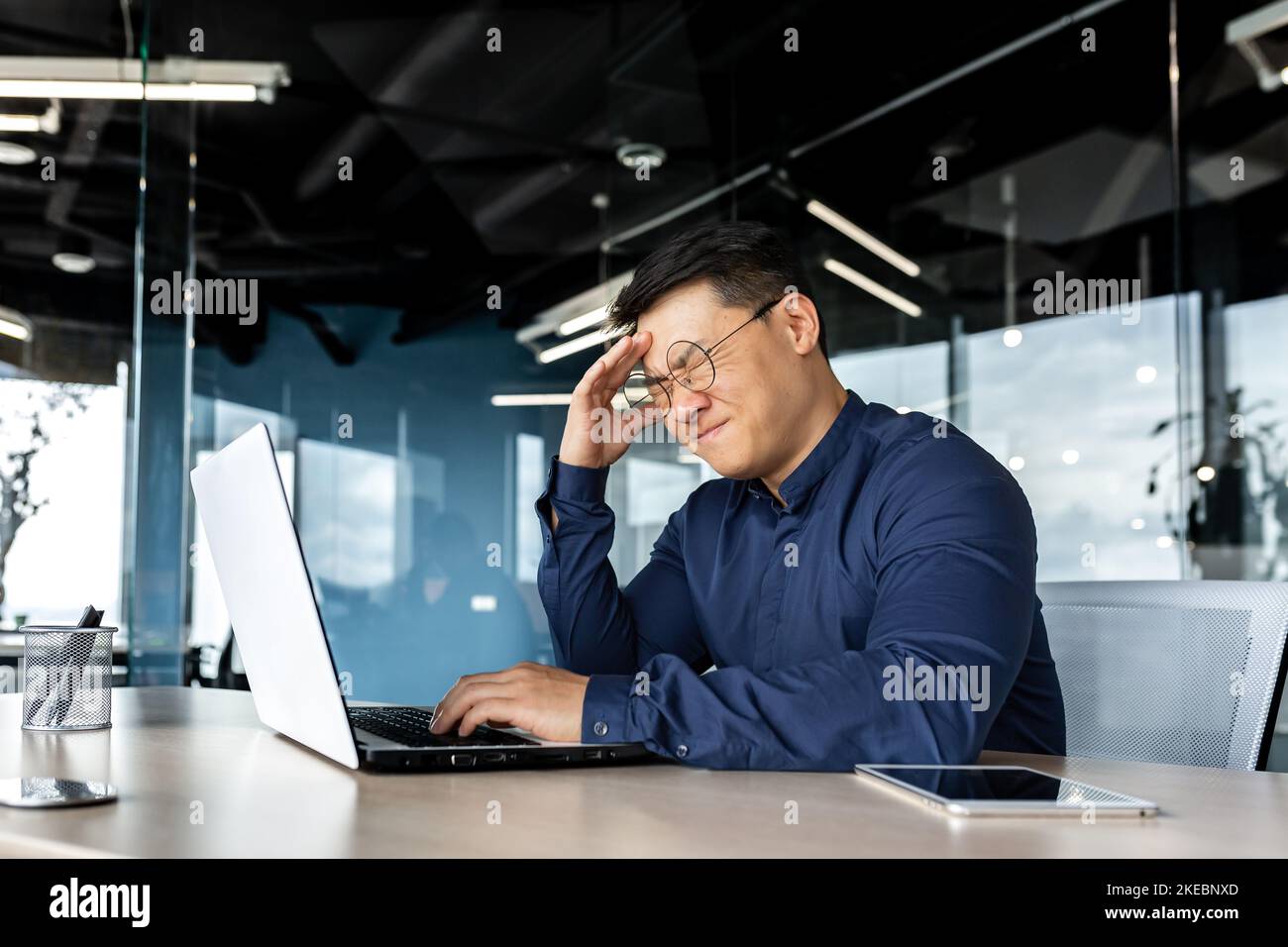 Uomo d'affari in occhiali depressi, l'uomo che tiene la testa ha ricevuto notizie di cattivo lavoro risultato, l'uomo asiatico deluso e triste lavorare in ufficio con il portatile. Foto Stock
