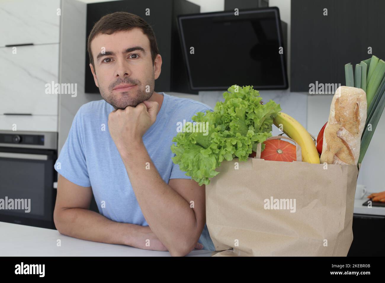 Uomo osservante soddisfatto con i generi alimentari sopra il bancone della cucina Foto Stock