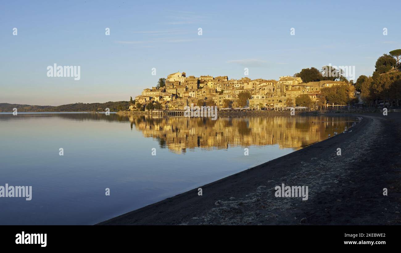 Anguillara Sabazia si riflette nelle acque del lago di Bracciano, illuminato dalla luce del tramonto Foto Stock