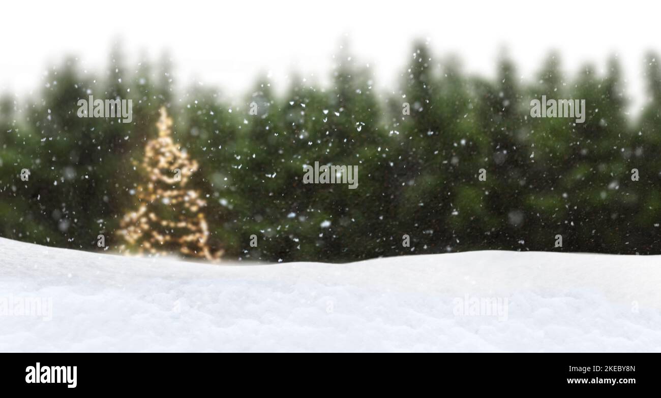 Albero di Natale con luci delle fate in nevicata di fronte alla foresta di abeti con sfondo sfocato Foto Stock