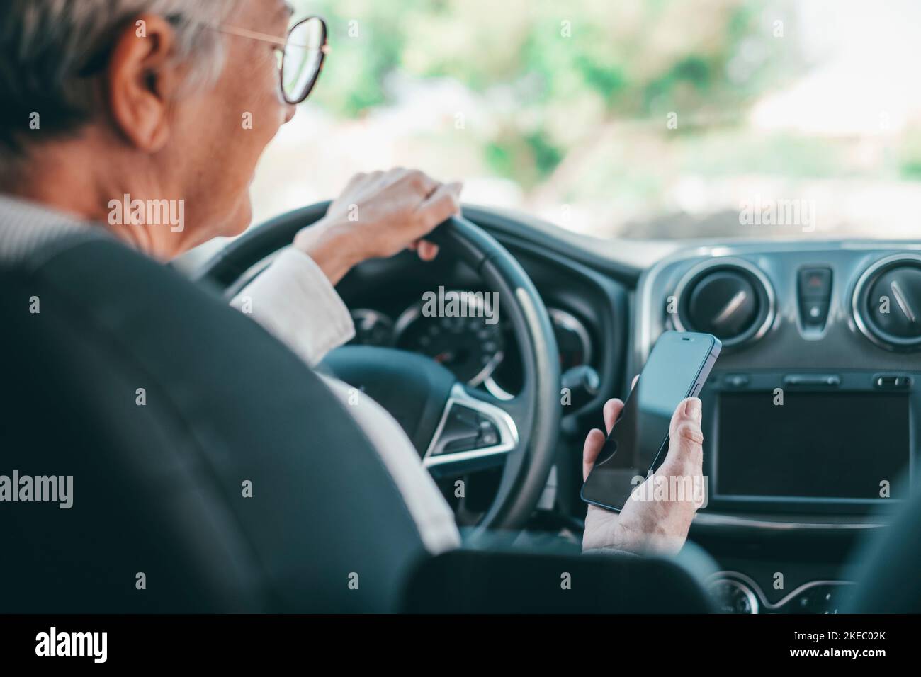 Ritratto di una donna anziana che utilizza il telefono in auto durante la guida su strada rischio di incidenti. Primo piano con lo smartphone per navigare in chat e inviare SMS online. Foto Stock