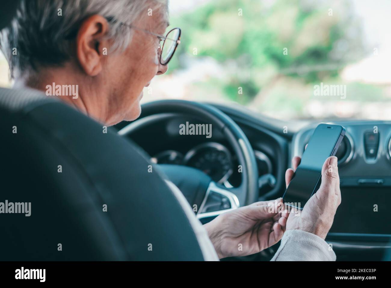 Ritratto di una donna anziana che utilizza il telefono in auto durante la guida su strada rischio di incidenti. Primo piano con lo smartphone per navigare in chat e inviare SMS online. Foto Stock
