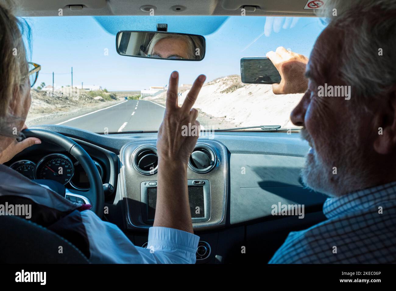 coppia di anziani e pensionati in auto guida e. prendere un selfie insieme sorridendo e guardando la fotocamera Foto Stock