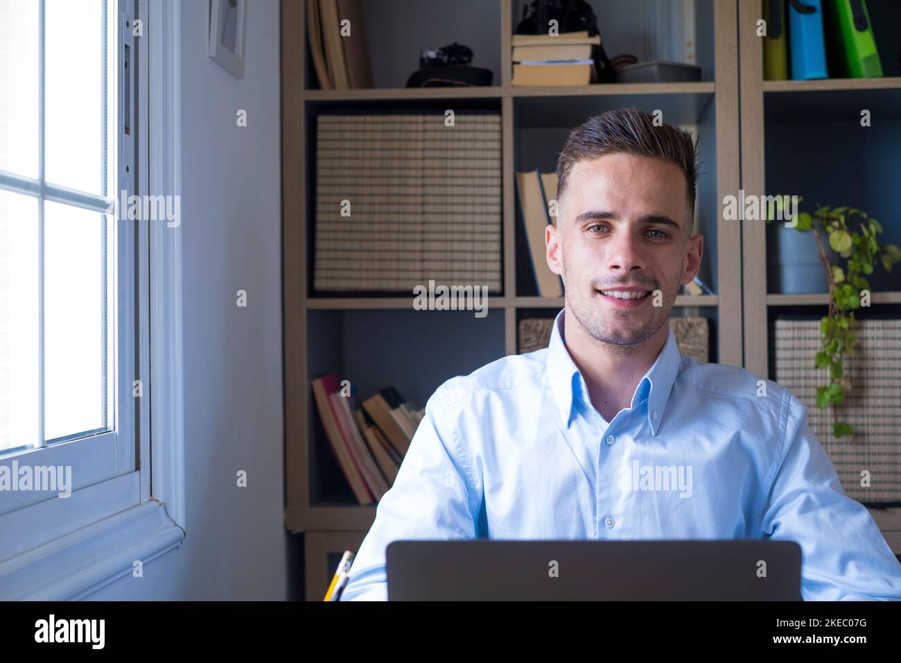 Ritratto di un bell'uomo d'affari sorridente con un computer portatile in ufficio. Giovane dirigente caucasico maschio guardando la fotocamera mentre lavora a casa. Uomo felice imprenditore al lavoro Foto Stock