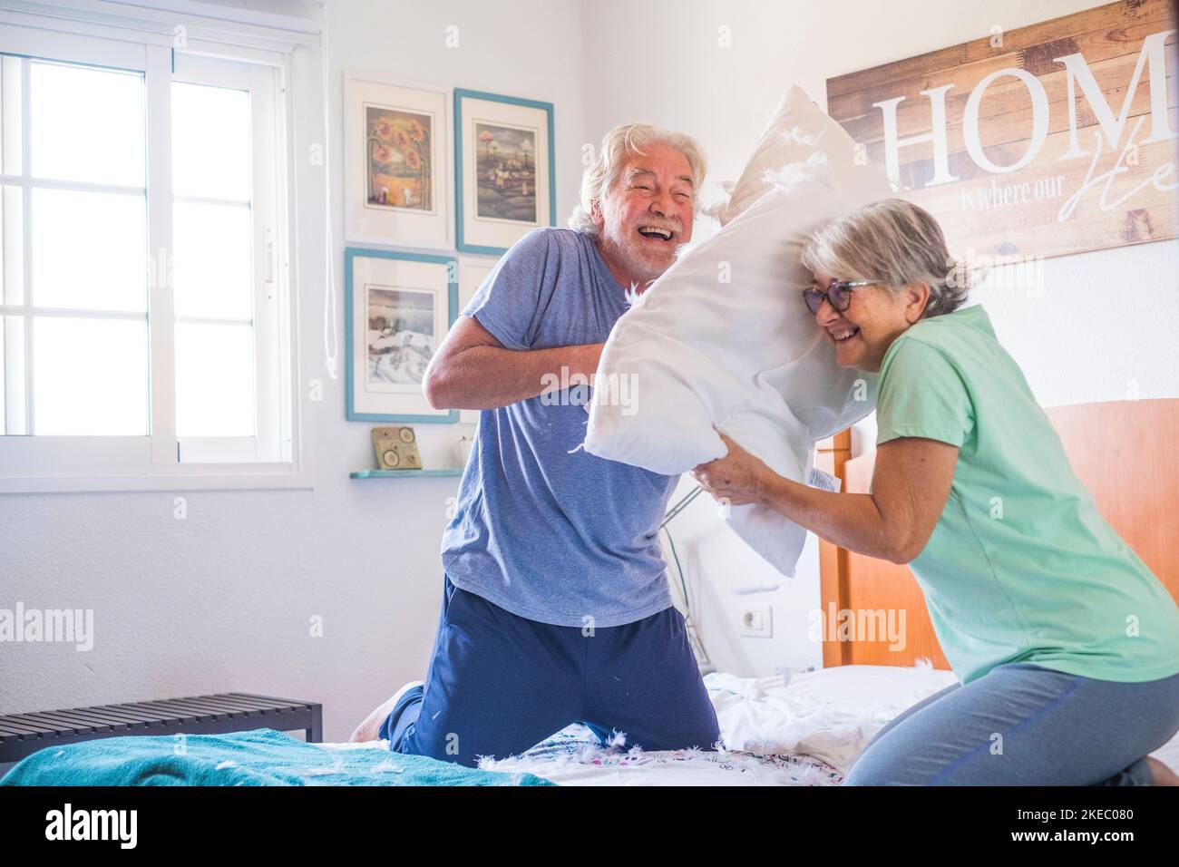 coppia di due anziani felici che si divertono a giocare insieme sul letto a casa lotta con cuscini godendo - cuscini guerra al coperto al mattino Foto Stock