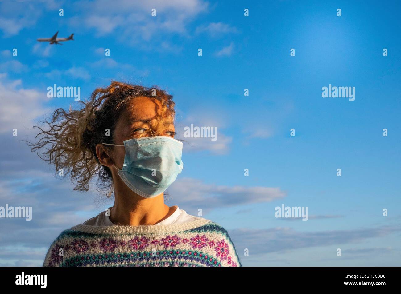 una donna riccia e bella che indossa una maschera medica per prevenire qualsiasi tipo di malattia o virus come coronavirus o covid-19 - aeroplano all'interno della sua testa sullo sfondo come pericolo di vacanze rischiose Foto Stock