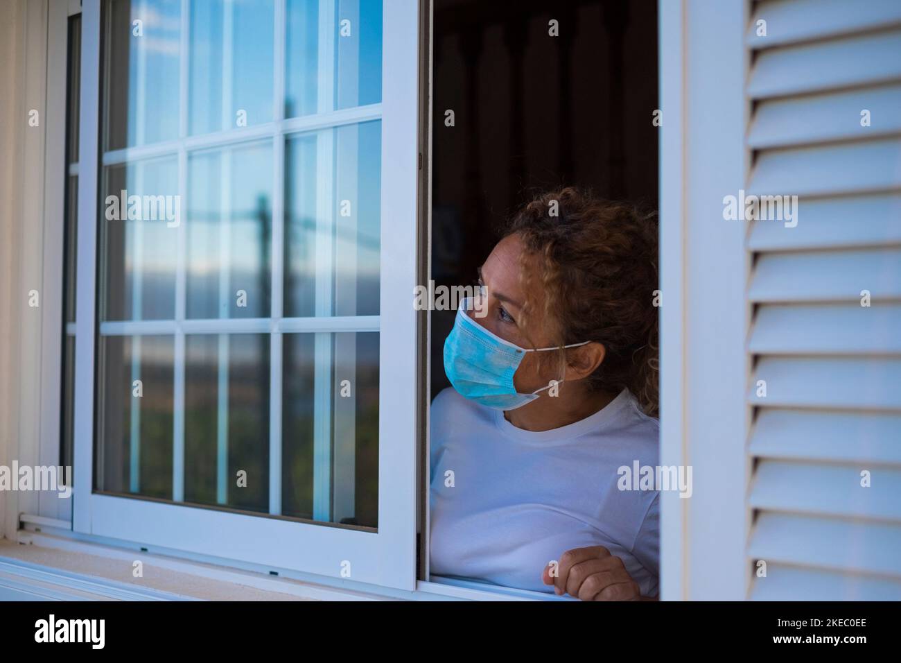 ritratto di donna che guarda all'aperto dalla finestra di lei casa in blocco o quarantena per essere al sicuro dal coronavirus o covid-19 - fase 1 o 2 di blocco Foto Stock