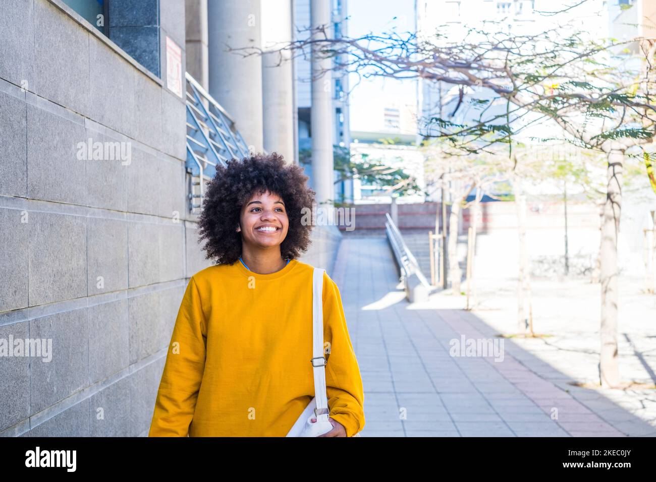 Primo piano ritratto di bella giovane donna nera sorridente all'aperto nella strada di una città grigia - donna d'affari a piedi e divertirsi da sola Foto Stock