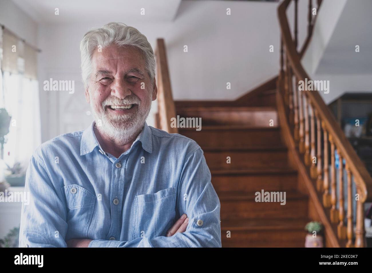 Buon vecchio con capelli grigi, anziano 80s sorridente con denti bianchi a casa. Ritratto di un nonno allegro rilassante al coperto. Foto Stock