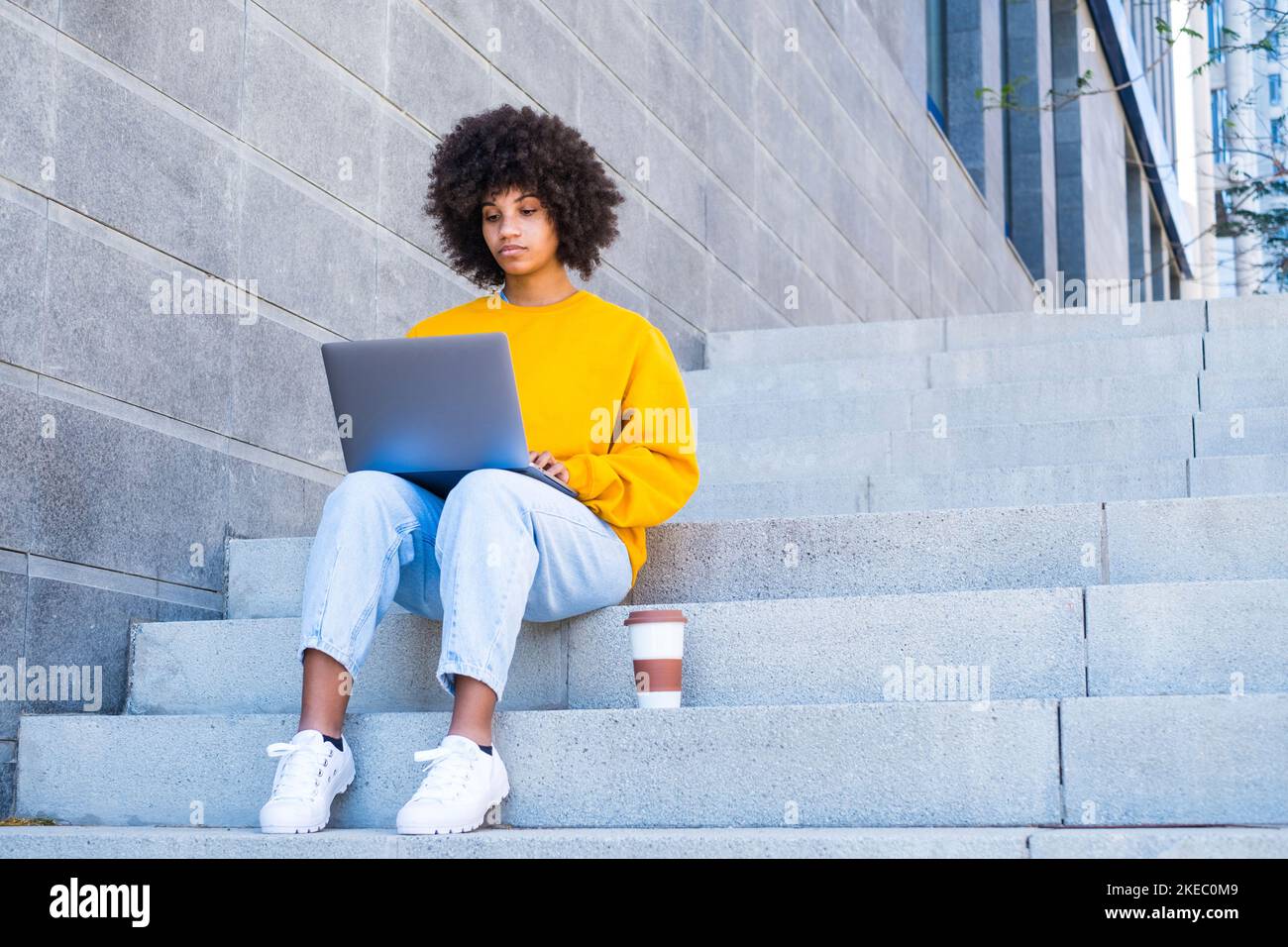 Felice giovane ragazza africana d'affari studente lavoratore relax sedersi sulle scale della città. Guardare lo schermo del notebook guardare i video online del webinar sul computer che si trova sul posto di lavoro finito il lavoro Foto Stock