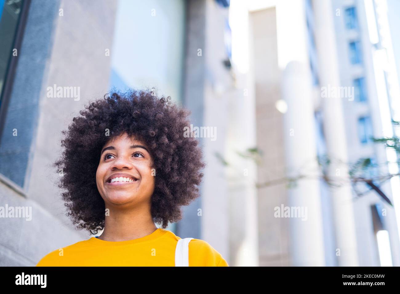 Primo piano ritratto di bella giovane donna nera sorridente all'aperto nella strada di una città grigia - donna d'affari a piedi e divertirsi da sola Foto Stock