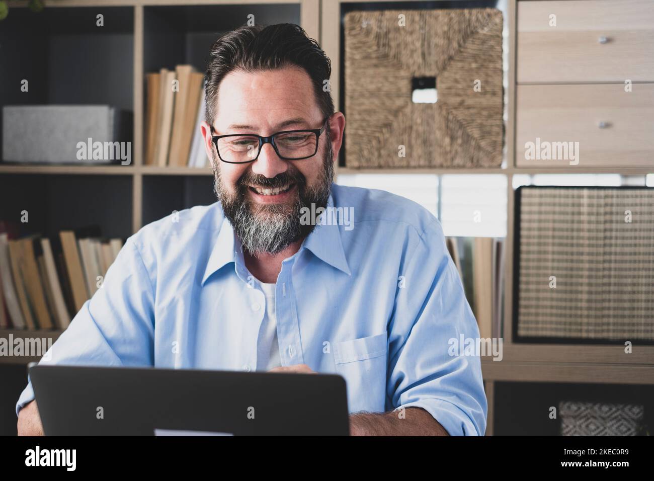 Sorridente freelancer maschile che lavora su un computer portatile seduto a casa ufficio, felice uomo d'affari maturo guardando lo schermo del computer che comunica online per il business, bell'uomo soddisfatto del successo online Foto Stock