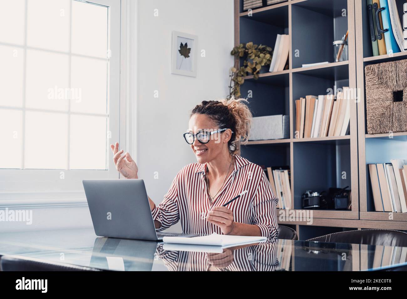 Una giovane donna che lavora a casa in ufficio con notebook e notebook prendendo appunti durante una videoconferenza. Una donna d'affari che chiama comunicare Foto Stock