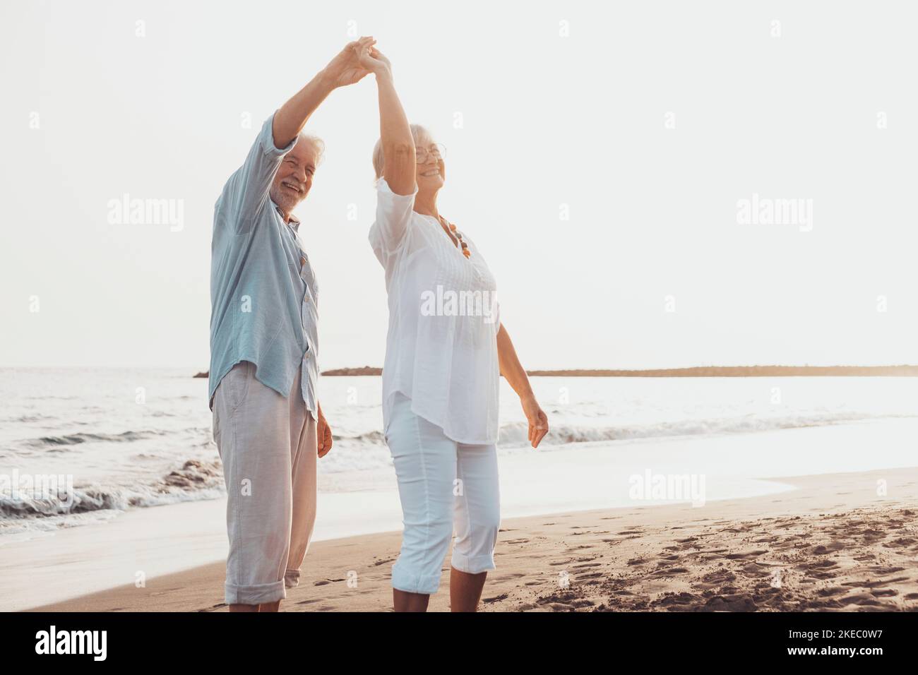 Coppia di persone anziane che ballano insieme e che si divertono sulla sabbia in spiaggia godendosi e vivendo il momento. Ritratto degli anziani innamorati che si guardano gli altri divertendosi. Foto Stock