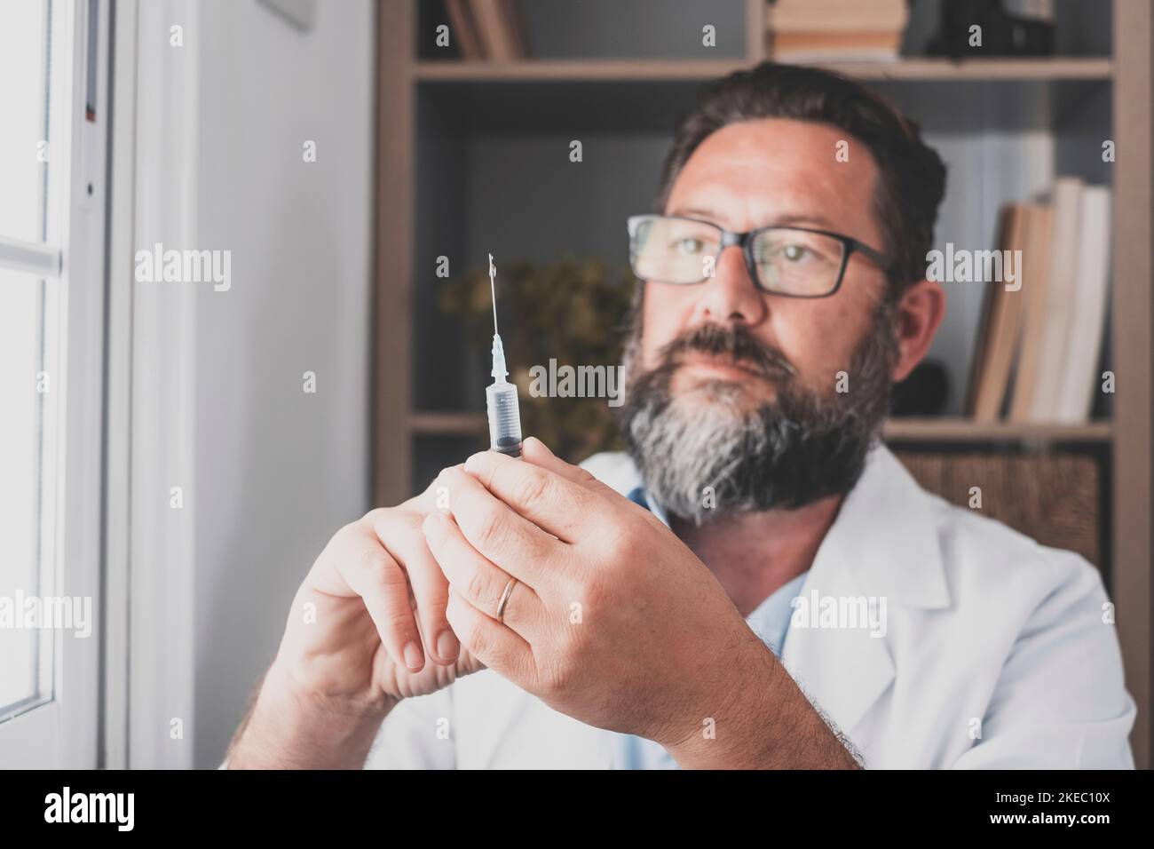 Primo piano e ritratto di infermiera di medico maschile in ufficio tenendo e mostrando una siringa grande per la fotocamera sorridente. Felice uomo con la vaccinazione nelle sue mani Foto Stock
