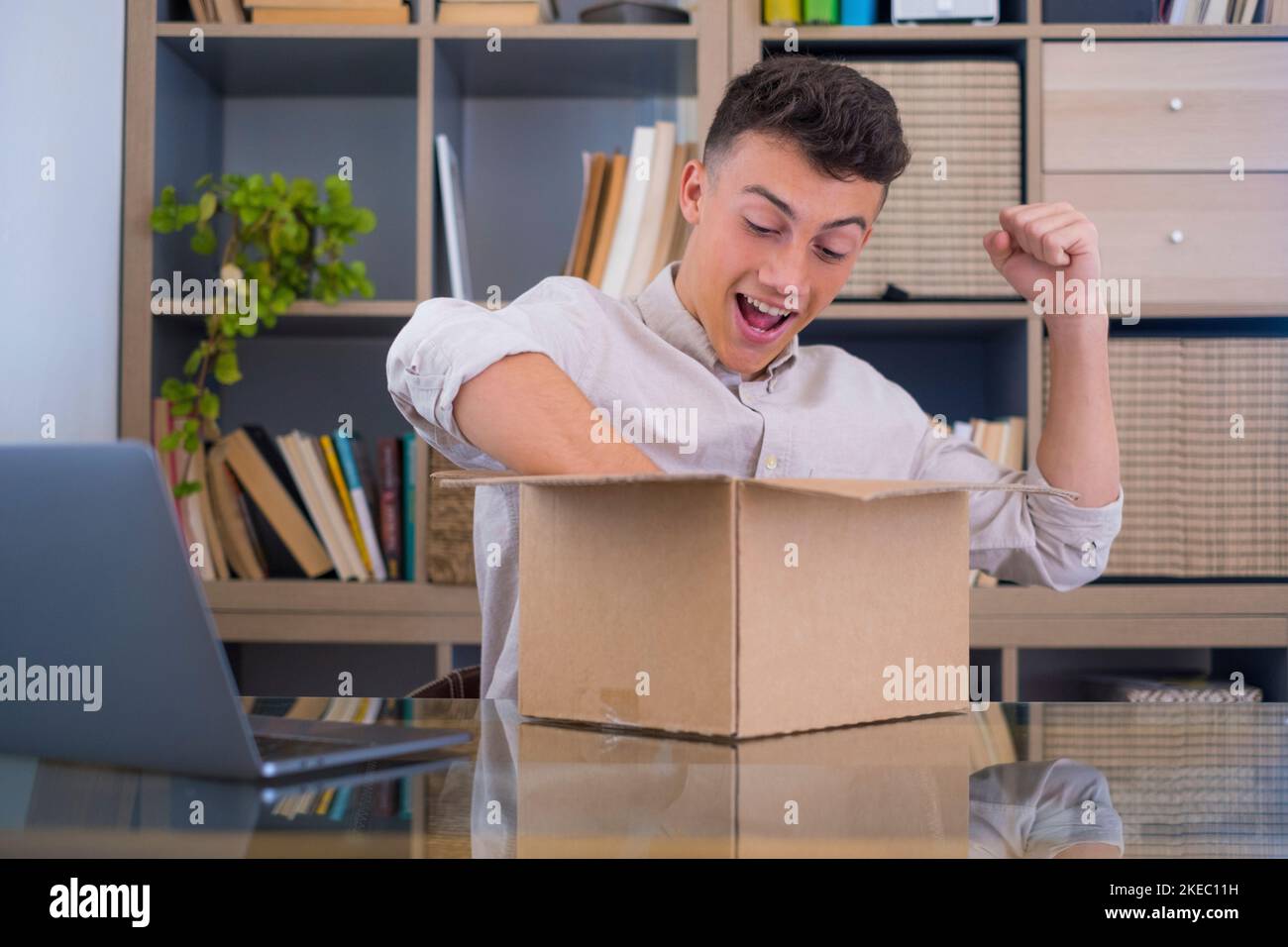 Uomo sorridente che indossa occhiali disimballaggio pacco atteso pacco, guardando all'interno, seduto alla scrivania, soddisfatto cliente felice apertura scatola di cartone con ordine negozio online, buon servizio di spedizione consegna Foto Stock