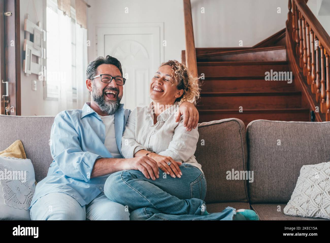 Felice coppia caucasica ridendo mentre si siede sul divano nel soggiorno. Marito e moglie ridono a casa a gran voce seduti sul divano. Uomo e donna che trascorrono del tempo libero in un appartamento moderno Foto Stock