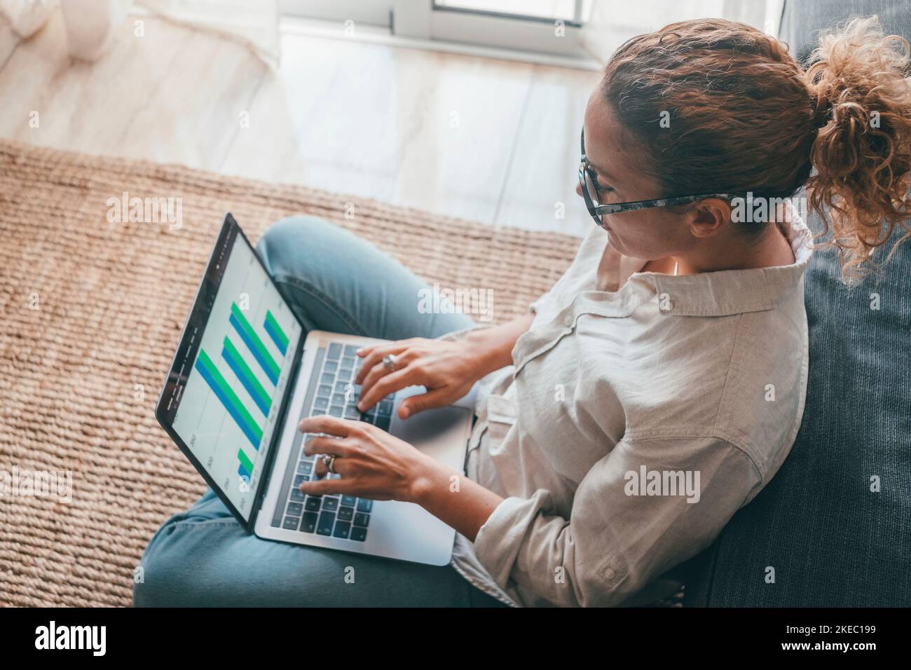 Primo piano vista posteriore giovane donna che utilizza il computer portatile e la calcolatrice, lavorando al progetto, controllando i documenti finanziari, seduto al tavolo a casa, guardando lo schermo del computer con i diagrammi, calcolando le fatture Foto Stock