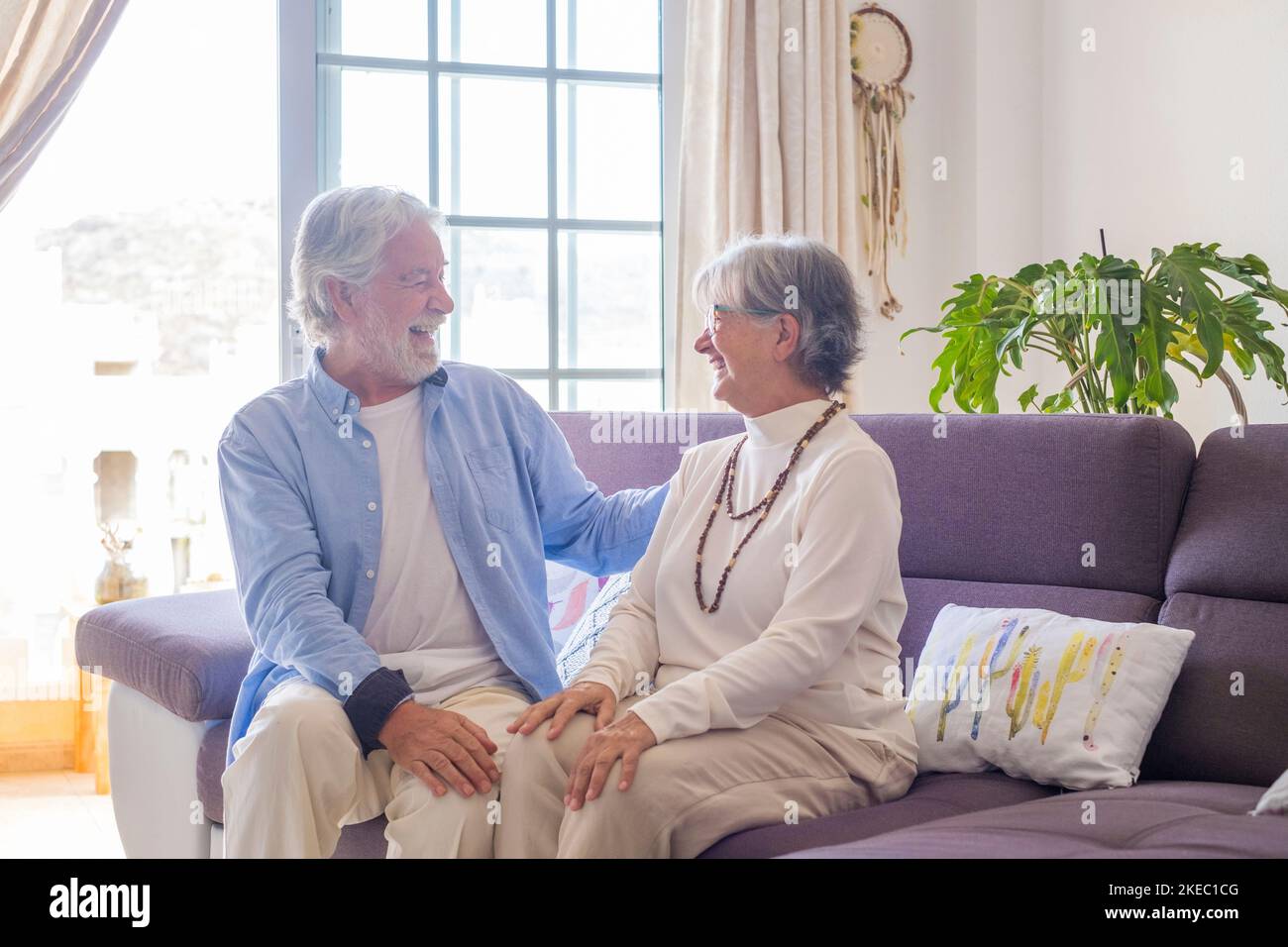 Ritratto di coppia di anziani ridendo e divertendosi seduti sul divano di casa in casa. Due persone anziane e mature sorridono e si divertono a scherzare. Foto Stock