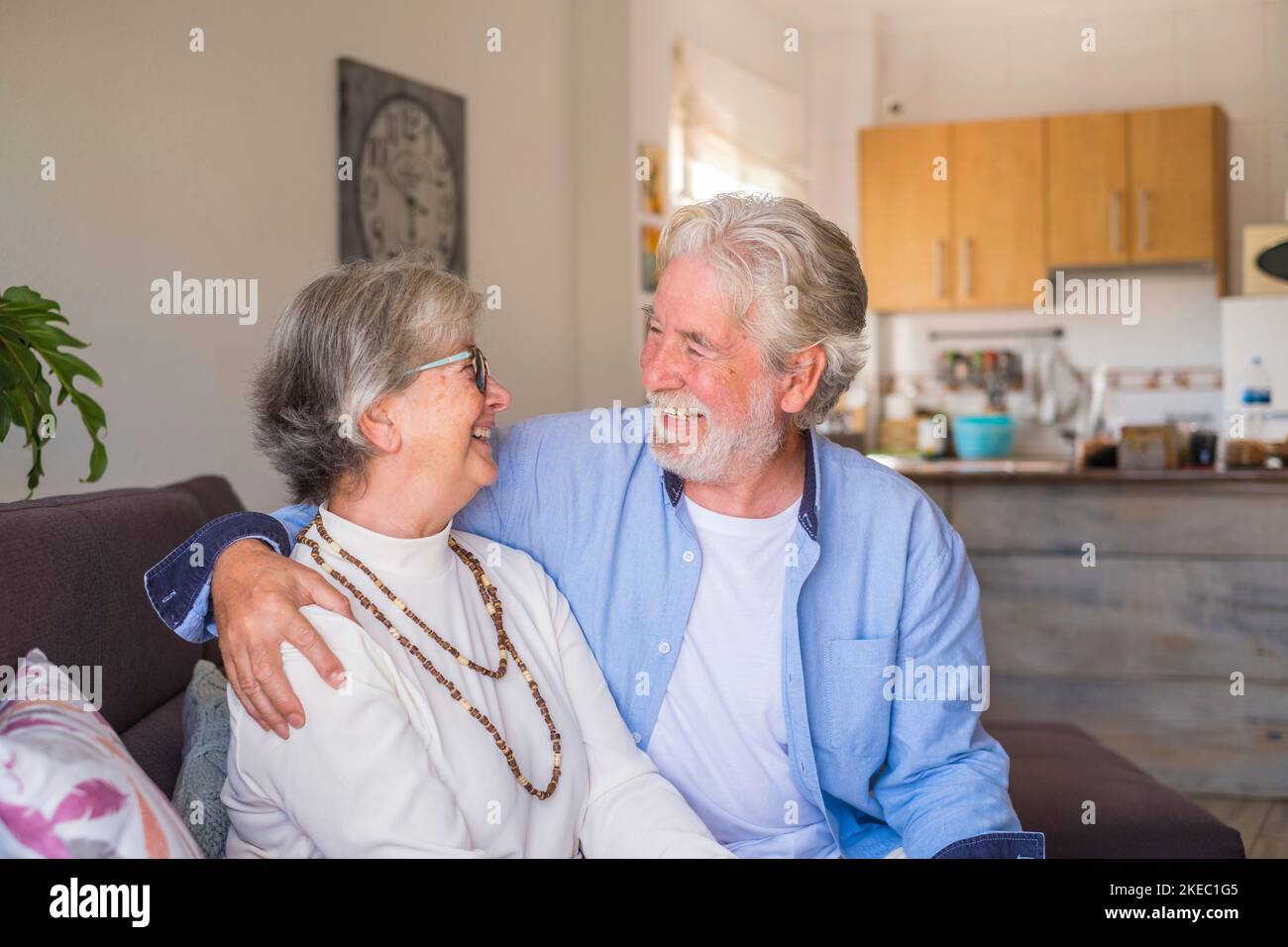 Ritratto di coppia di anziani ridendo e divertendosi seduti sul divano di casa in casa. Due persone anziane e mature sorridono e si divertono a scherzare. Foto Stock