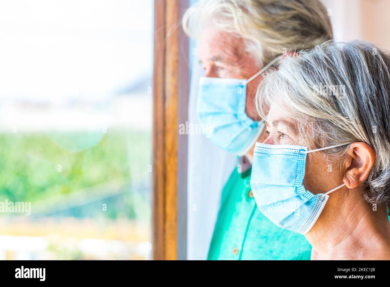Coppia di due persone anziane e mature che guardano all'aperto dalla loro casa indoor indossare maschera per prevenire coronavirus - stile di vita di blocco Foto Stock