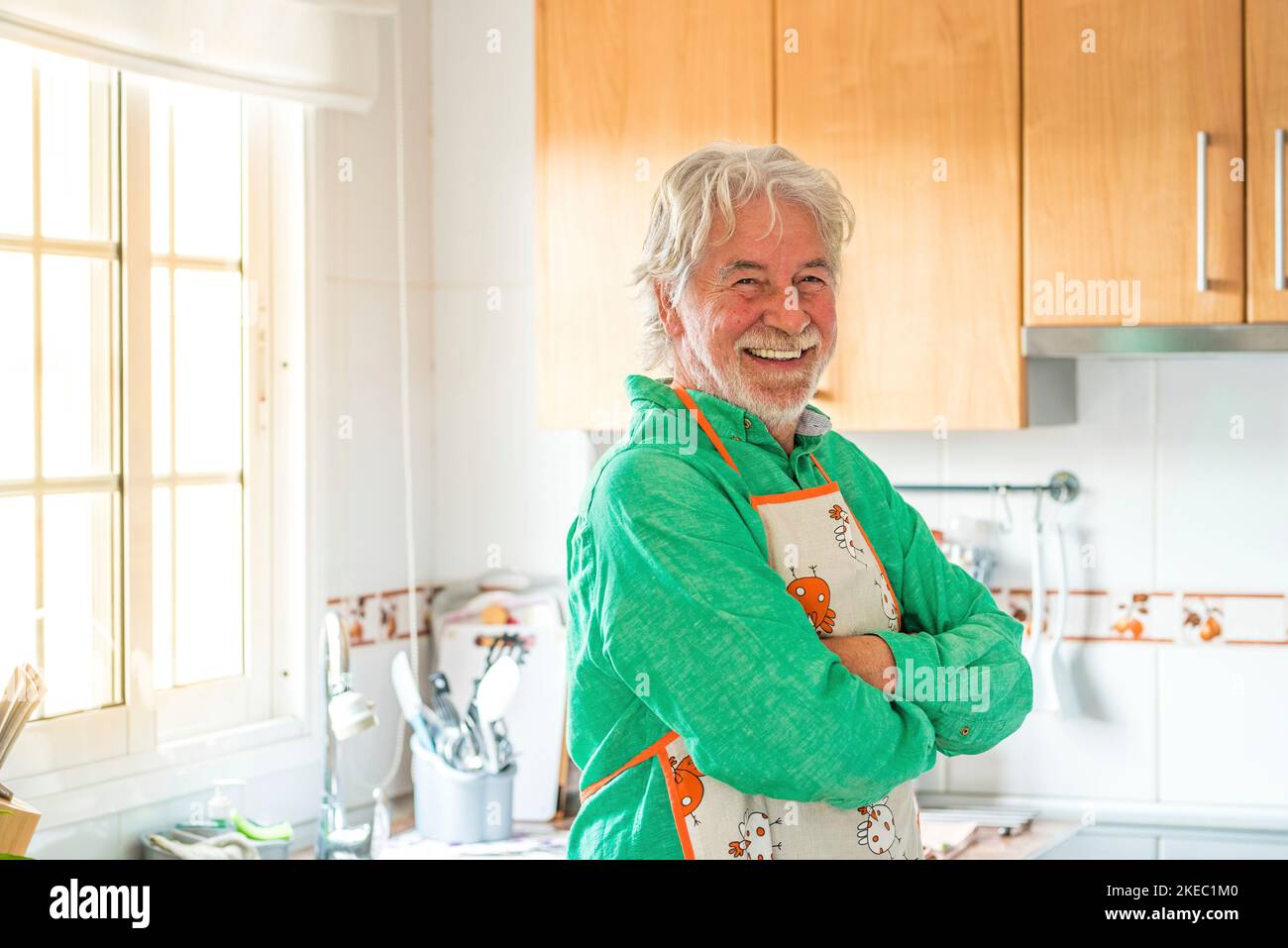 ritratto di un uomo maturo o anziano sorridente e guardando la macchina fotografica che cucina in cucina a casa Foto Stock