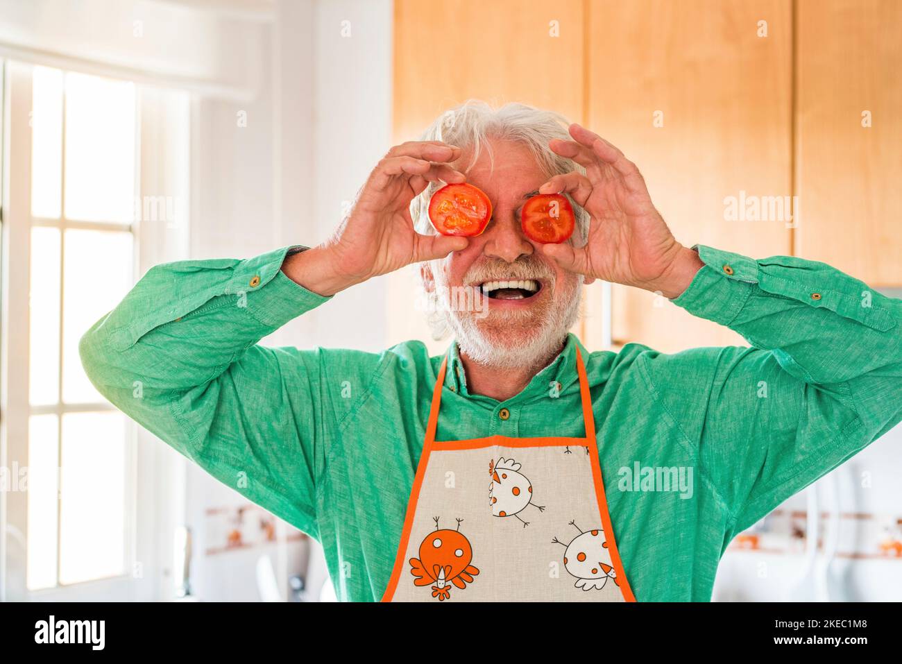 ritratto di un uomo anziano o maturo ridendo e sorridendo guardando la macchina fotografica cucinando e con due pomodori sugli occhi che fanno un volto Foto Stock