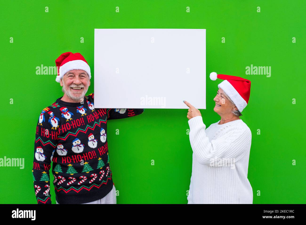 due vecchio e uomo maturo che tiene uno spazio vuoto o un grande scheet con uno spazio di copia per scrivere il tuo testo - vestiti di natale e sfondo verde Foto Stock