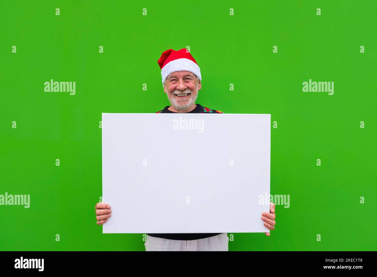 un uomo vecchio e maturo che tiene uno spazio vuoto o un grande scheet con uno spazio di copia per scrivere il vostro testo - vestiti di natale e sfondo verde Foto Stock