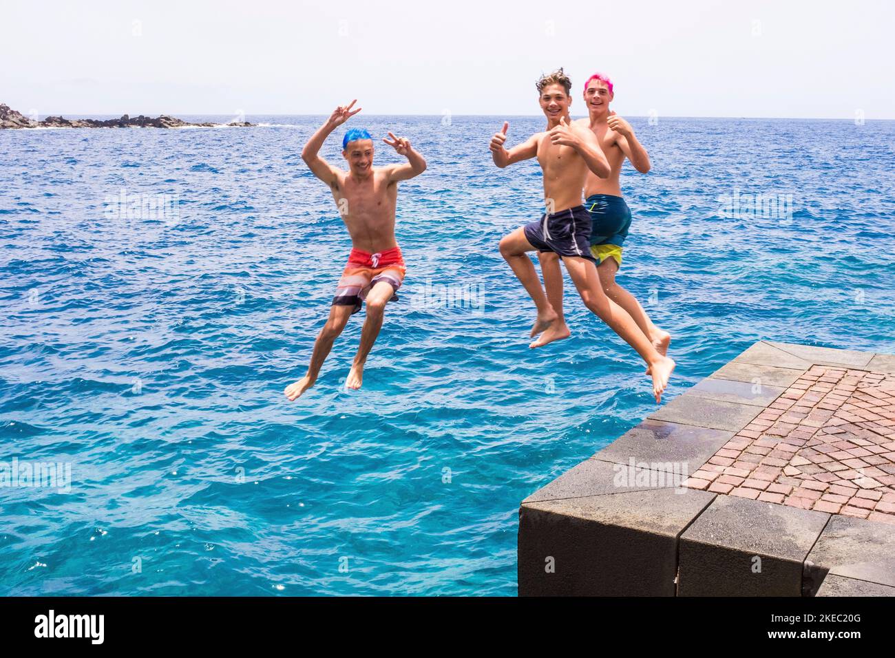 gruppo di amici che saltano insieme in spiaggia facendo capovolgimenti e divertendosi in acqua - la gente godendo la loro vacanza in spiaggia giocando e ridendo - guardando la macchina fotografica mentre saltano Foto Stock
