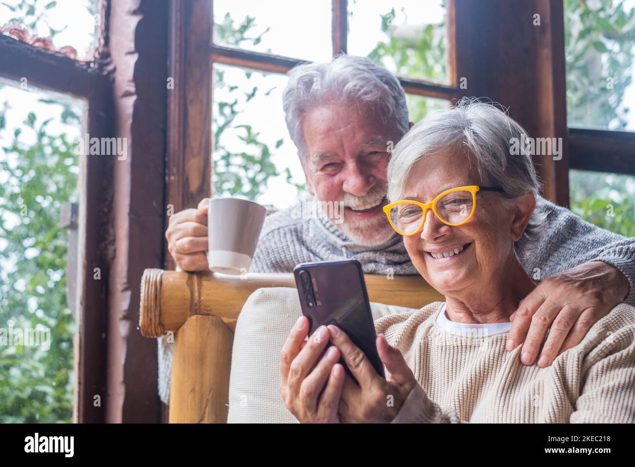 Coppia di due persone anziane e mature a casa utilizzando il telefono insieme nel divano. Smartphone per uso senior divertente e divertente da guardare. Concetto di tempo libero e libero nel soggiorno Foto Stock