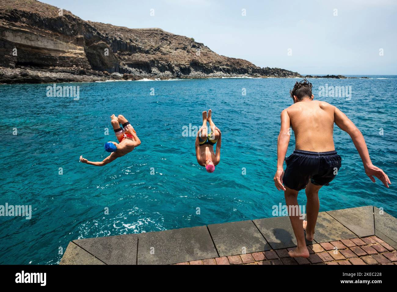 gruppo di amici che saltano insieme in spiaggia facendo capovolgimenti e divertendosi in acqua - la gente godendo la loro vacanza in spiaggia giocando e ridendo Foto Stock