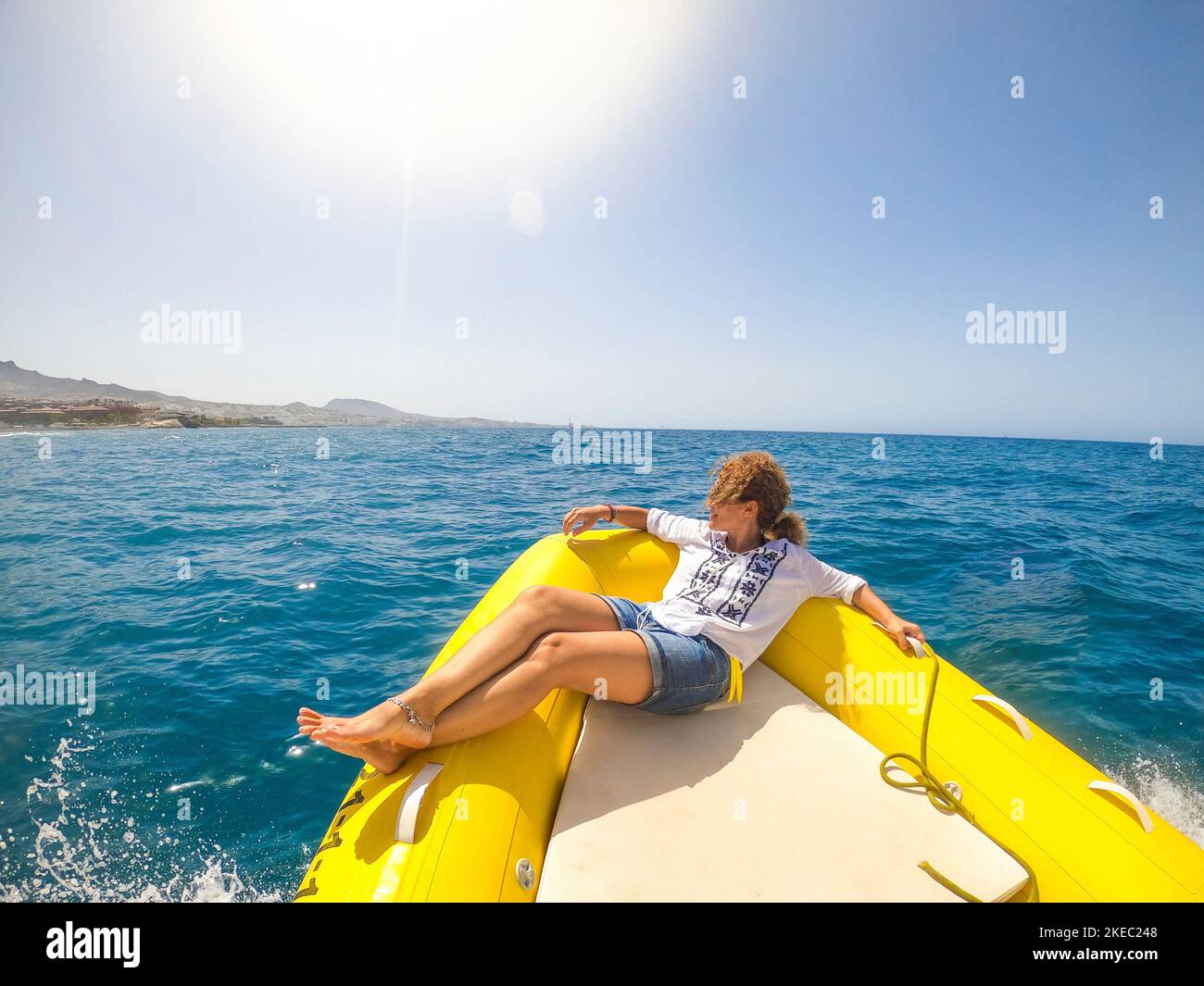 una giovane donna sdraiata su una barca che viaggia alla scoperta del mare godendosi e rilassandosi con una giornata di sole - guardando la costa dal gommone Foto Stock