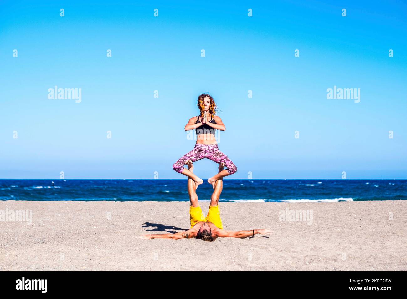 coppia di due adulti sani e in forma fisica che fanno esercizi insieme alla spiaggia sulla sabbia - due persone che fanno acro yoga Foto Stock