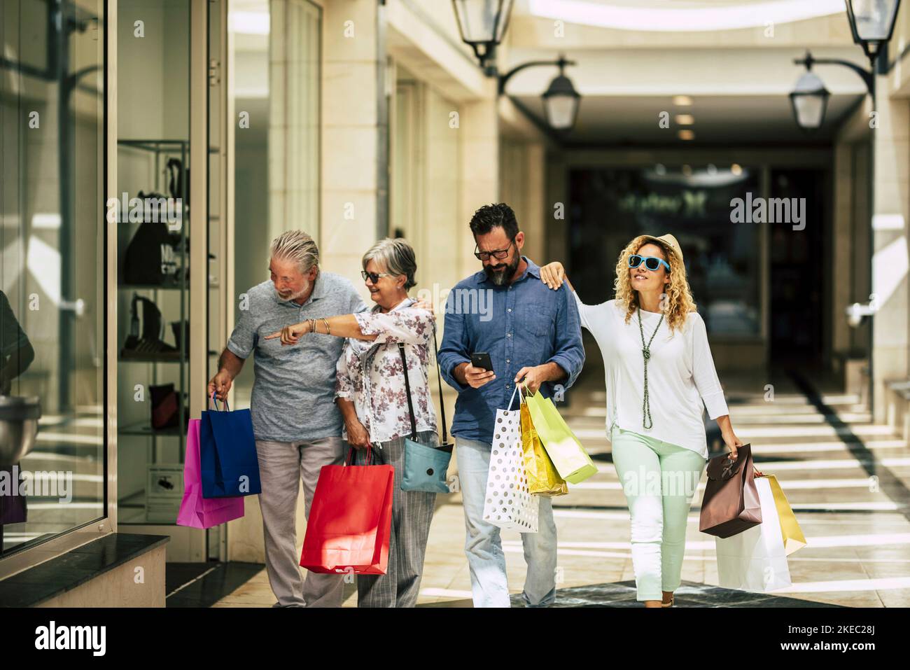 gruppo di persone che vanno a fare shopping insieme al centro commerciale con borse per lo shopping - due anziani e una coppia di adulti in cerca di negozi Foto Stock