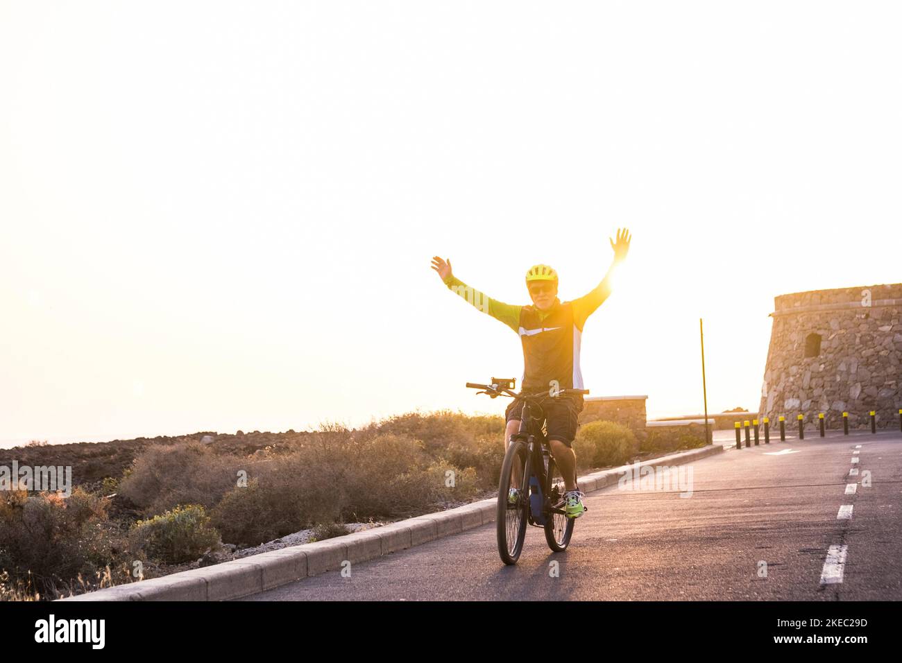 un uomo maturo e pensionato che si diverte in bicicletta da solo per strada con il tramonto sullo sfondo - fitness e stile di vita sano del vecchio adulto - andare in bicicletta e divertirsi a braccia aperte come concetto di libertà Foto Stock