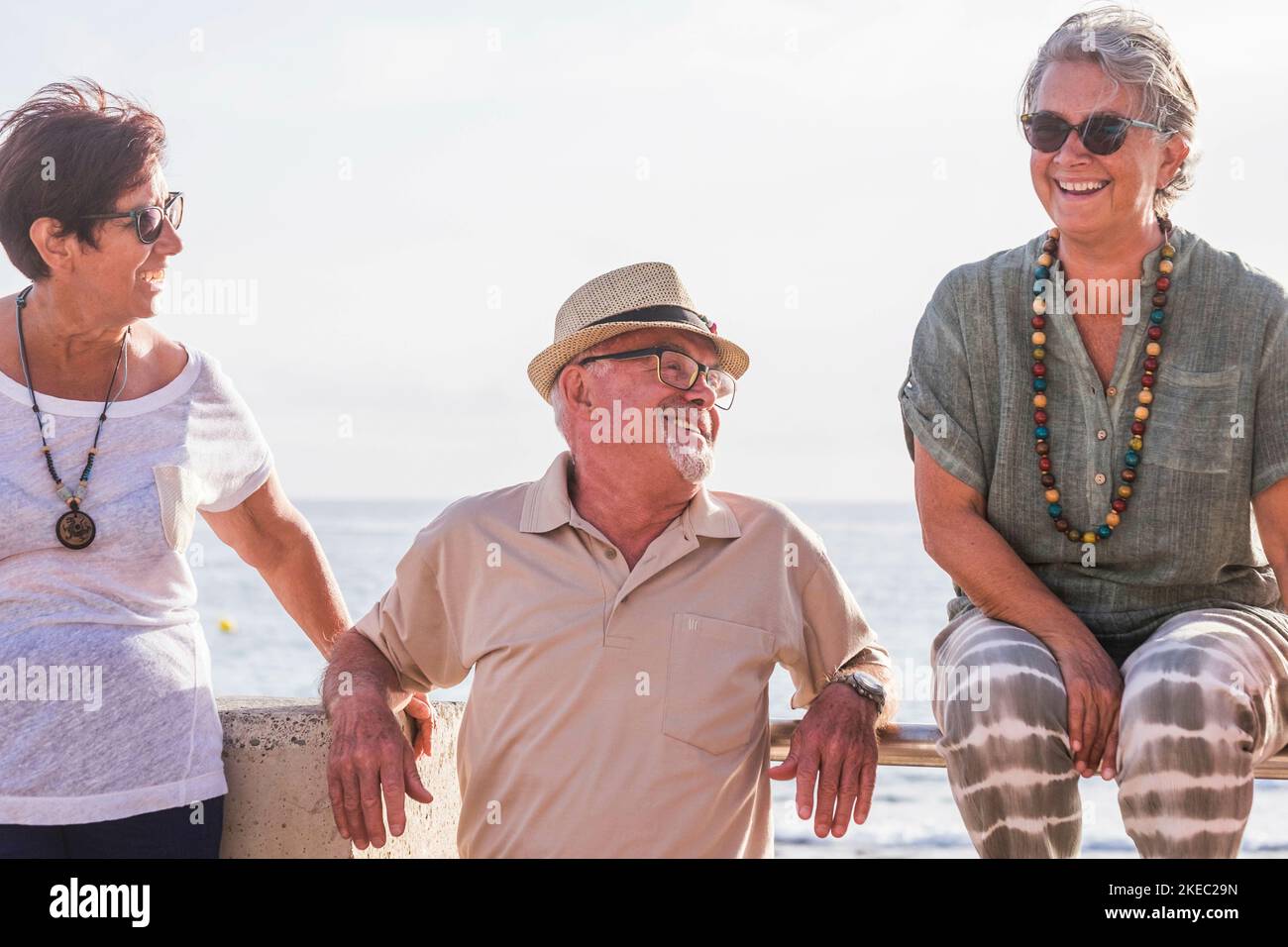 gruppo di tre anziani che si divertono insieme ridendo e sorridendo con la spiaggia sullo sfondo - due donne e. un uomo Foto Stock