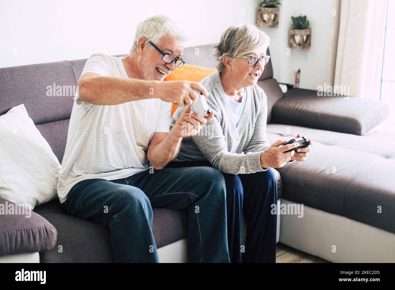 coppia di persone anziane e mature che guardano la tv e usano i controller che giocano insieme a casa i videogiochi sul divano - stile di vita chiuso al chiuso Foto Stock