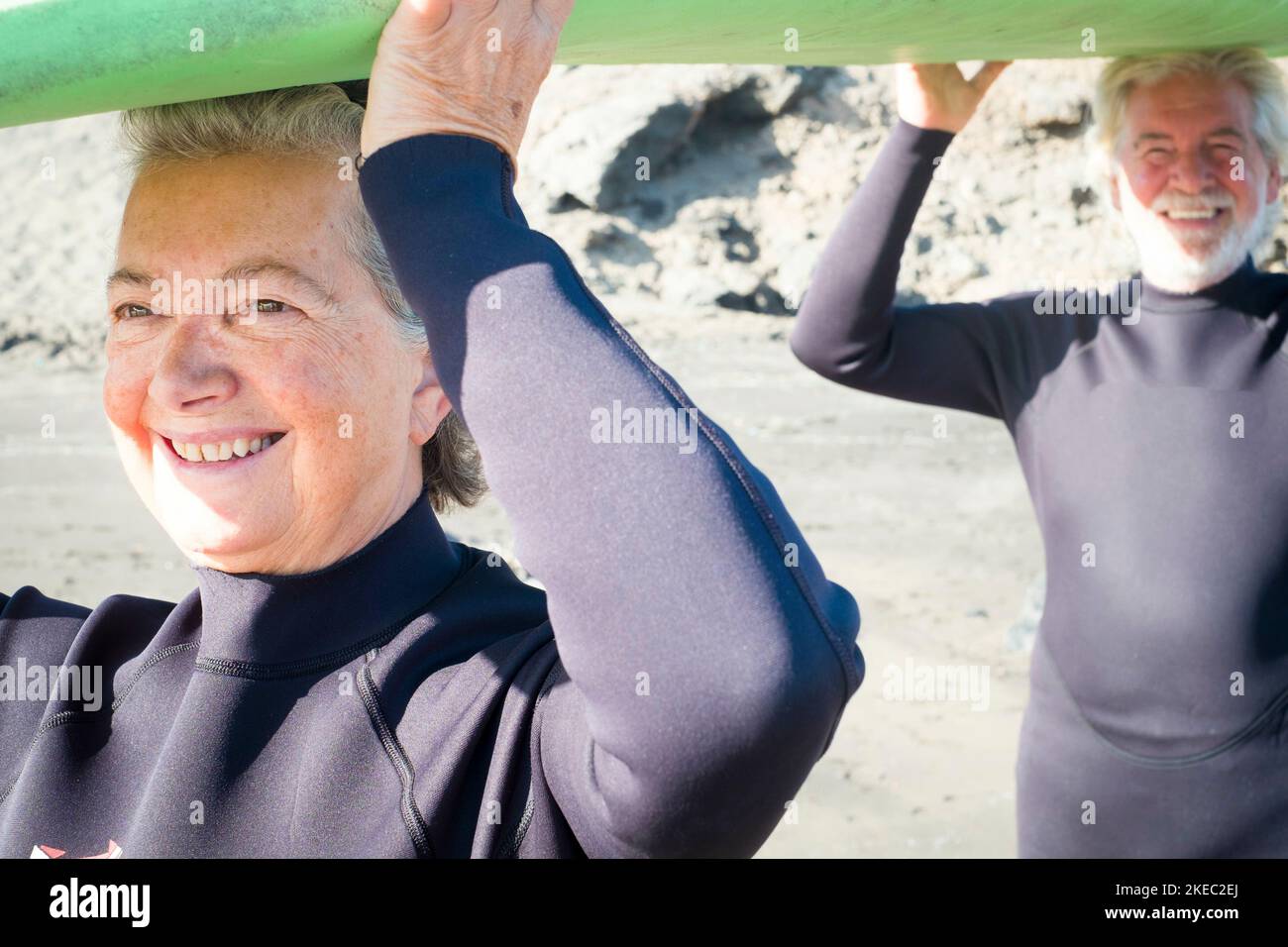 primo piano di due anziani che tengono insieme una tavola da surf per andare a fare surf e divertirsi - persone attive e mature pronte a provare e imparare a fare surf Foto Stock