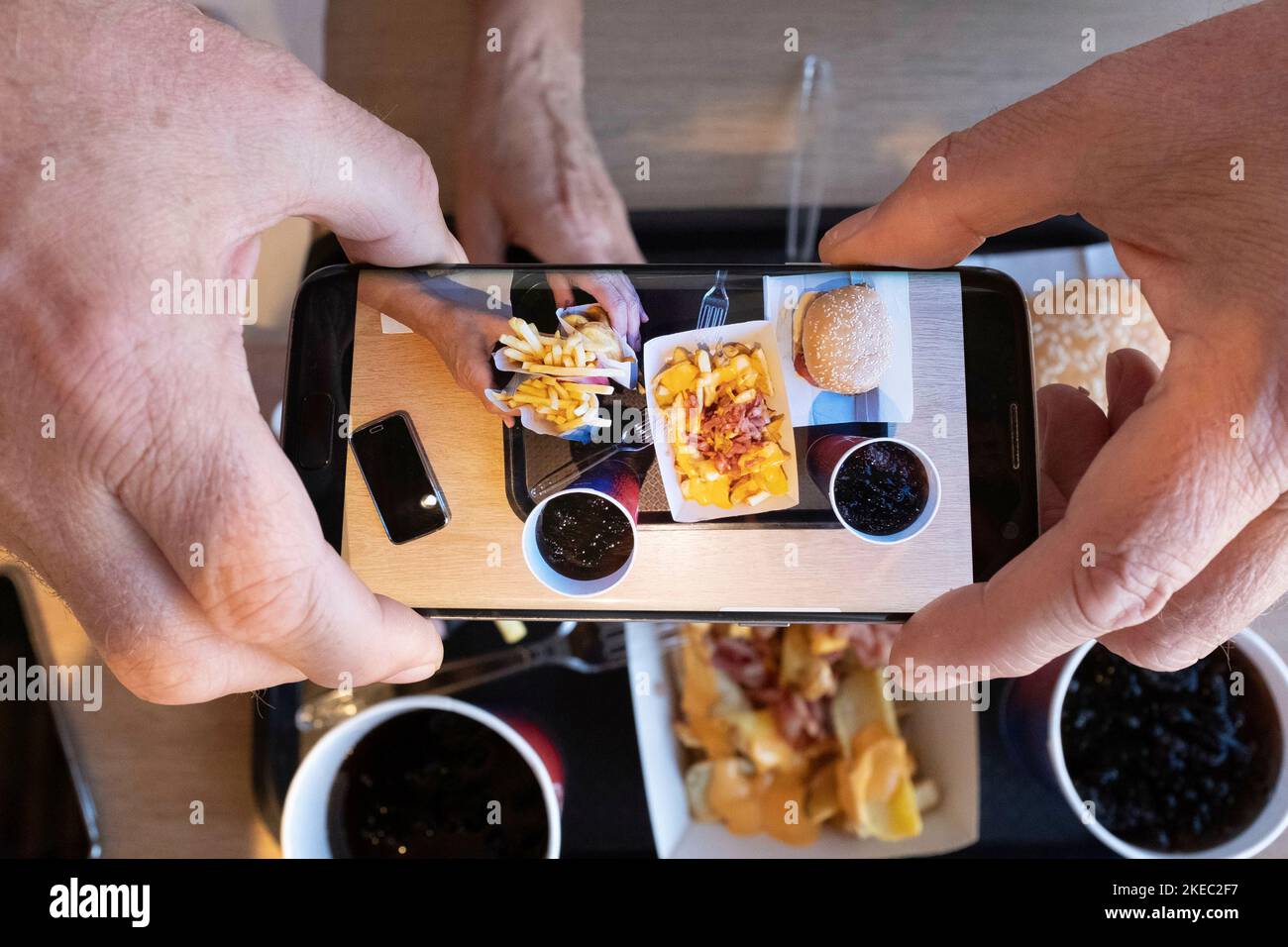 Concetto di persone anziane e tecnologia moderna con primo piano delle mani dell'uomo che scattano foto al cibo sul tavolo - spazzatura nnutrizione hamburger e stile di vita sano persone Foto Stock