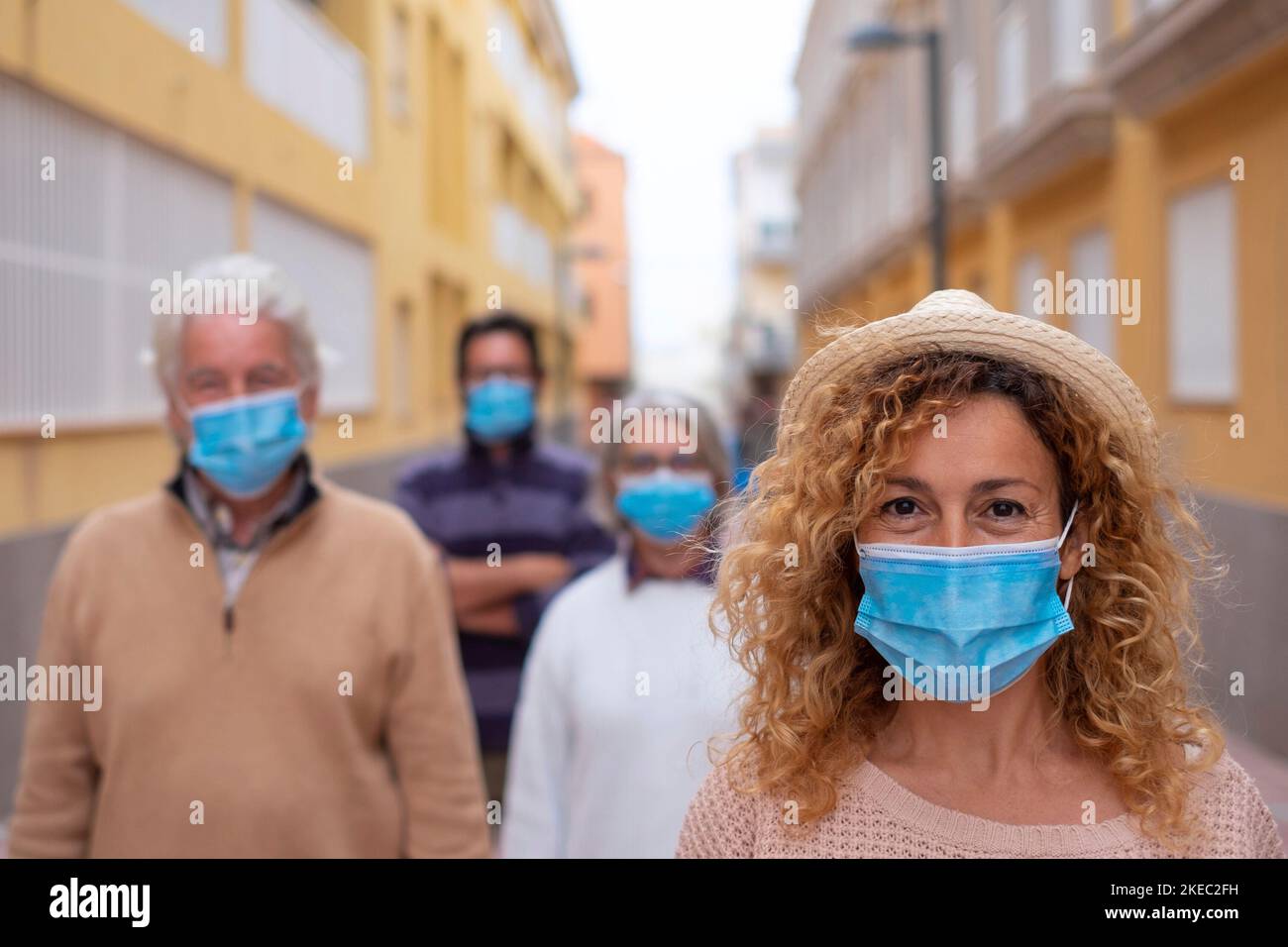 gruppo di quattro persone che indossano maschera mediale e chirurgica e respirano la distanza sociale insieme per strada - adulti sorridenti e che guardano la macchina fotografica in stile di vita pandemico Foto Stock