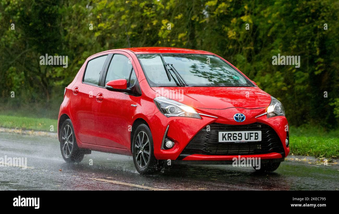 2019 rosso ibrido elettrico Toyota Yaris guida sotto la pioggia su una strada bagnata Foto Stock