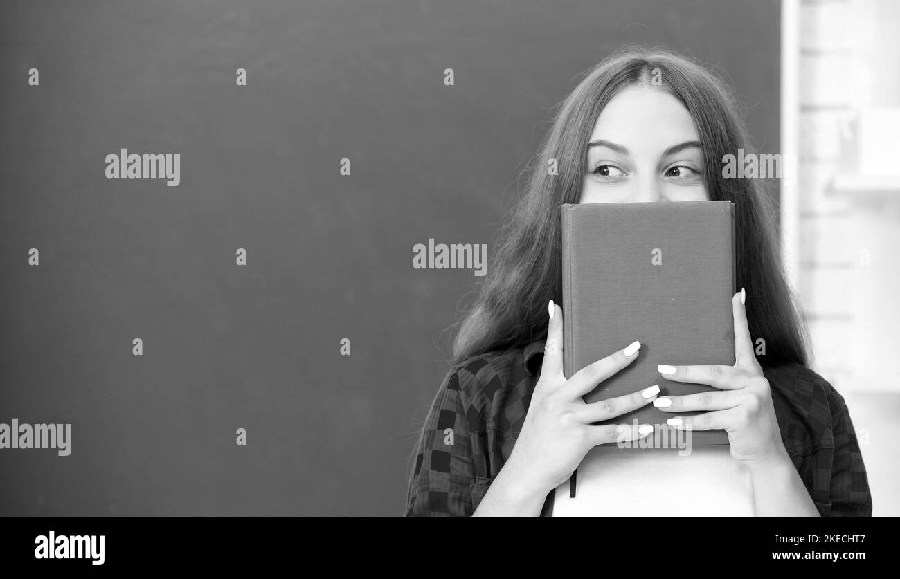 teen girl in high school nascondersi dietro il libro degli esercizi alla lavagna, istruzione Foto Stock